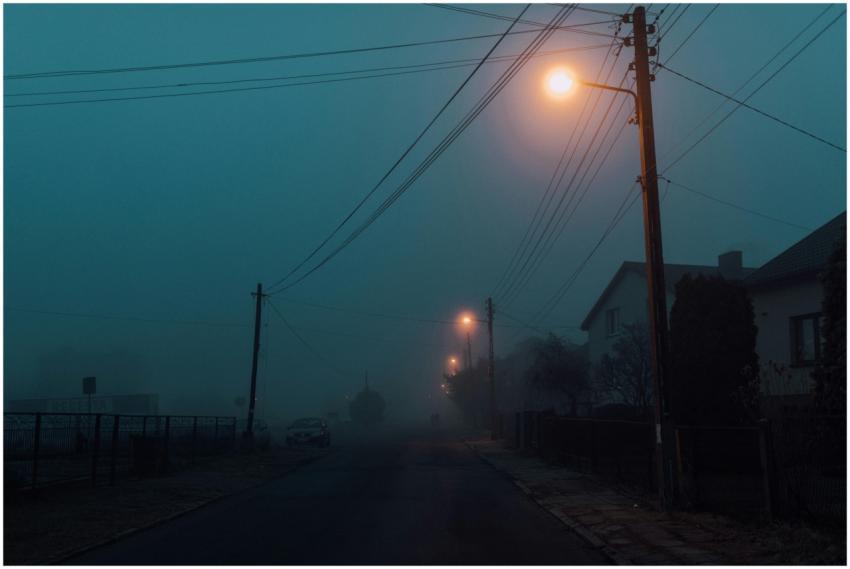 A foggy street illuminated by streetlights creates