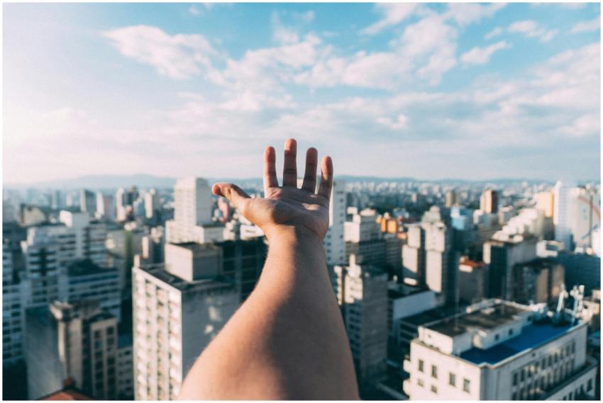 An outstretched hand reaching towards a sunny city
