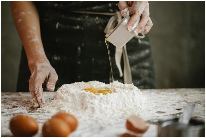 Chef pouring oil into flour and egg mix for homema