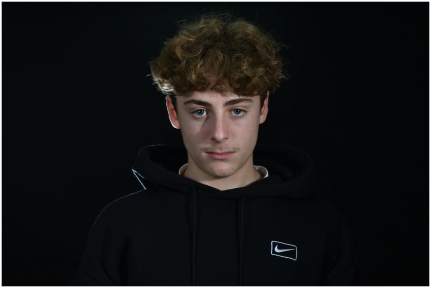 Young man with curly hair and black hoodie against