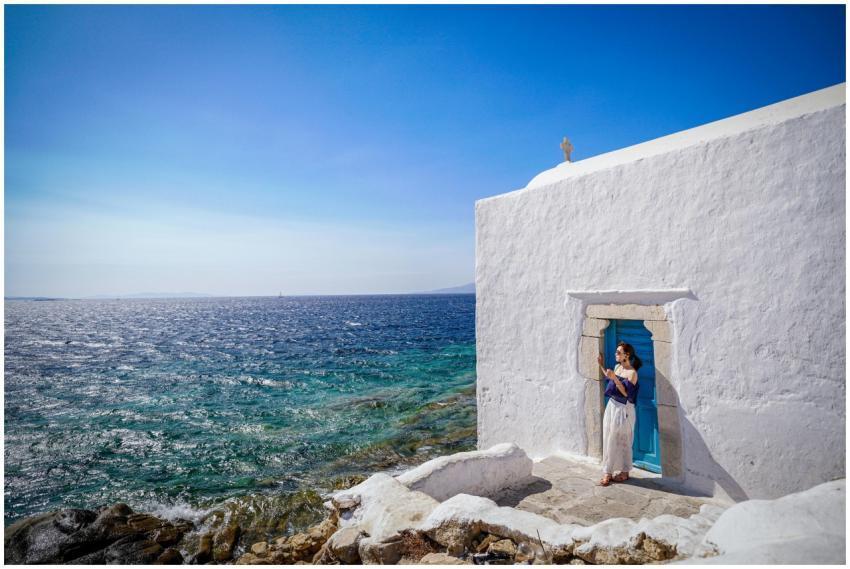 A woman in summer attire stands by a white chapel