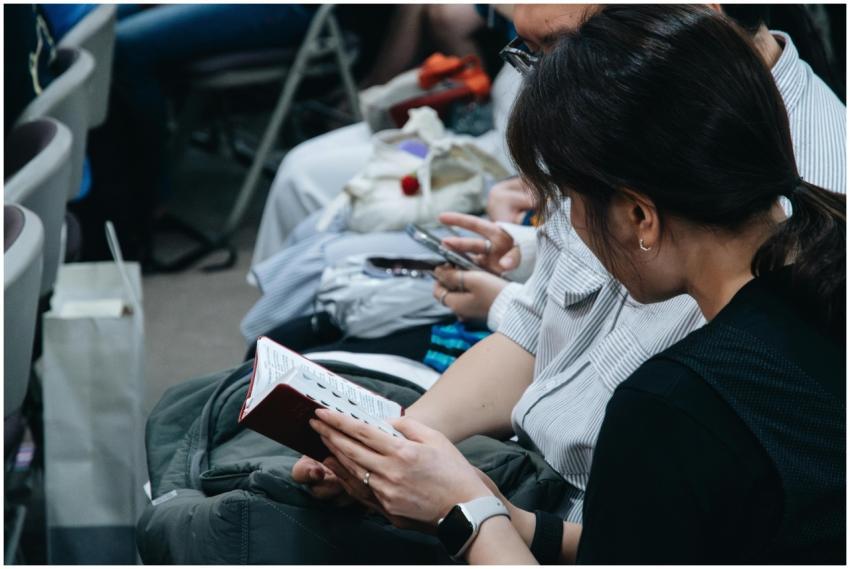 Close-up of people sitting in a crowd, reading a b