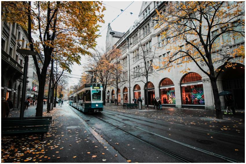 A tram travels down a leaf-strewn street in autumn