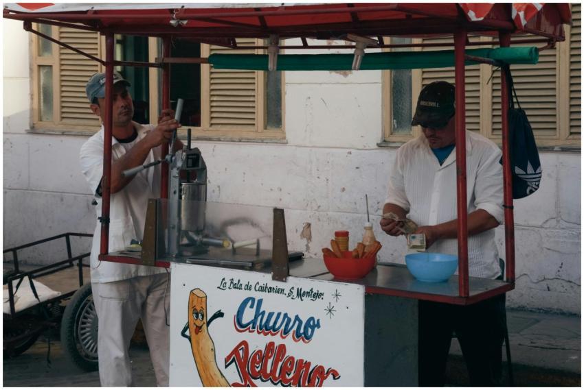 Two men operate a churro stand in a busy urban are