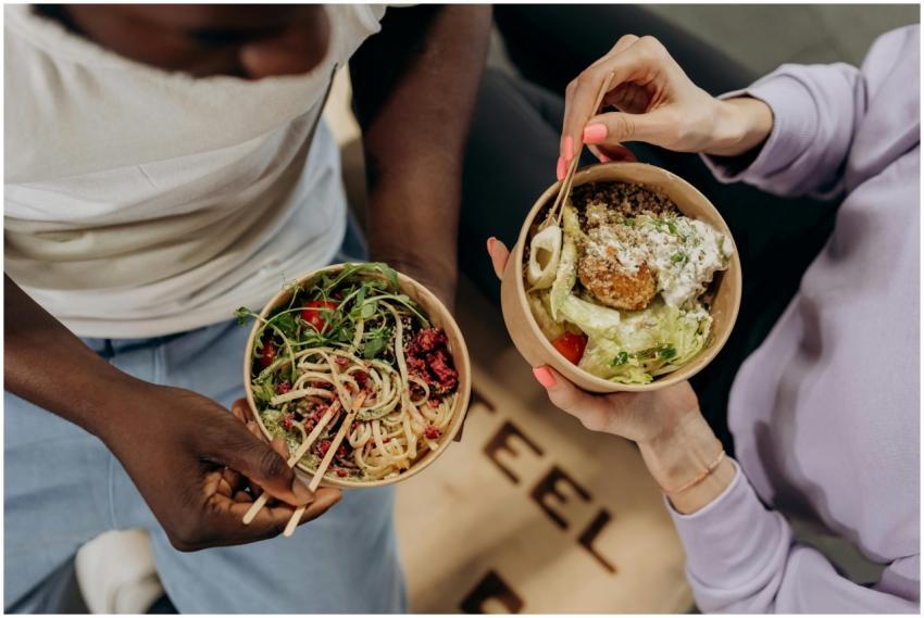 Two people holding bowls filled with salad and pas