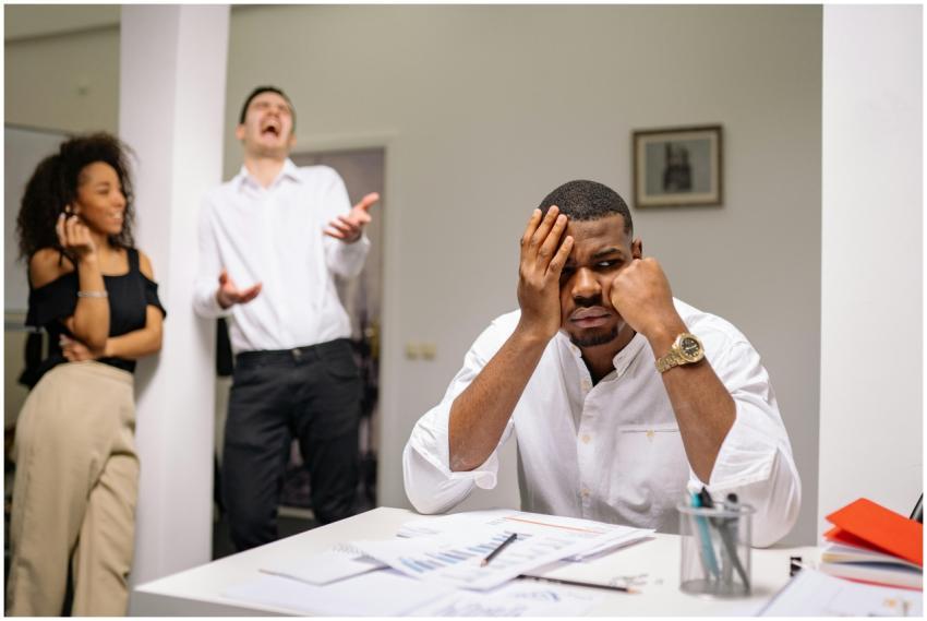 A man at a desk looks frustrated while two coworke