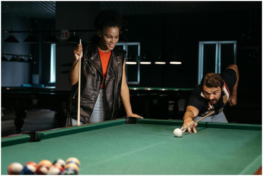 Two friends enjoy a game of billiards in a dimly l