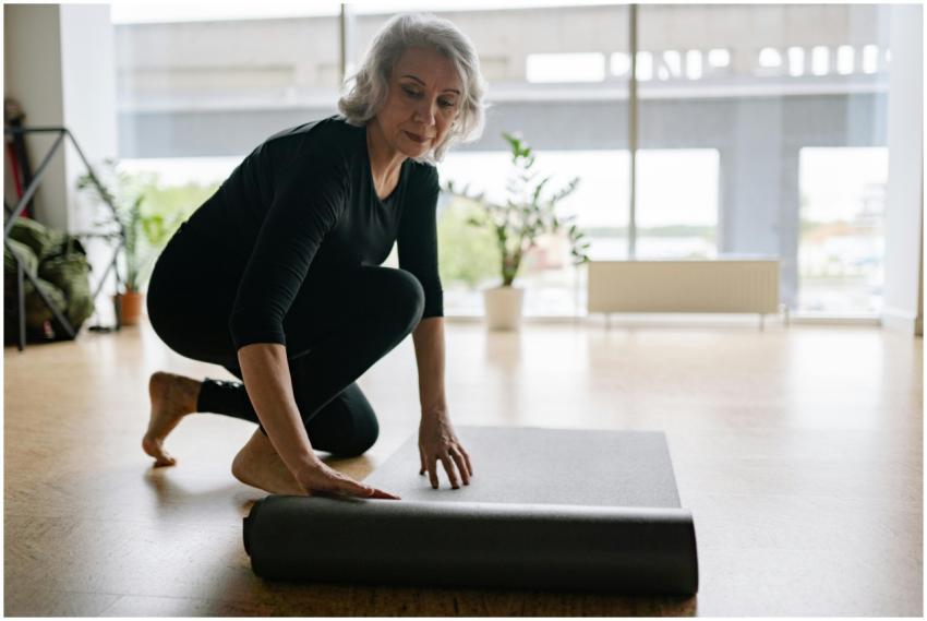 Senior woman setting up yoga mat in bright studio,