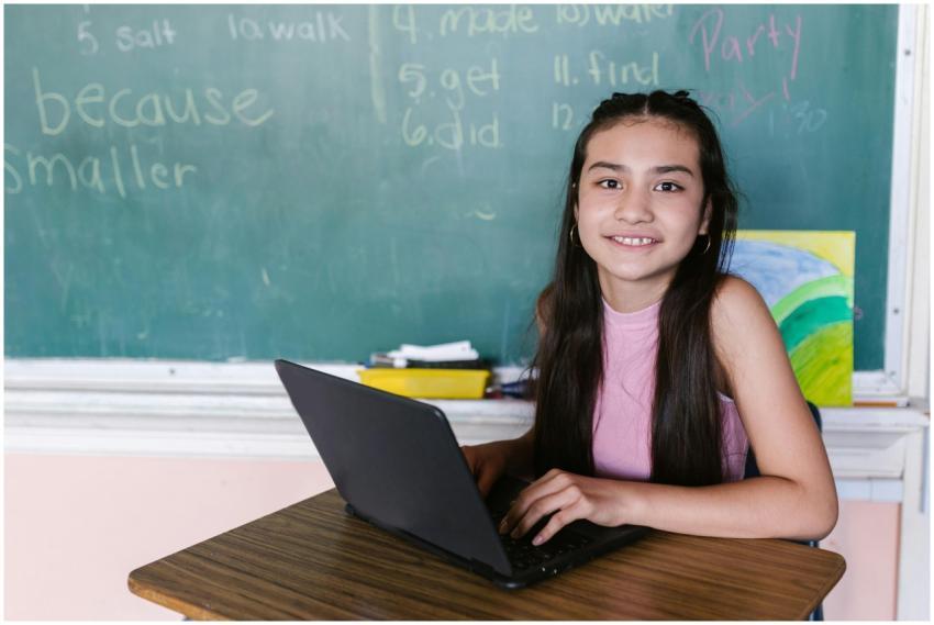 Young girl in a classroom, smiling while using a l