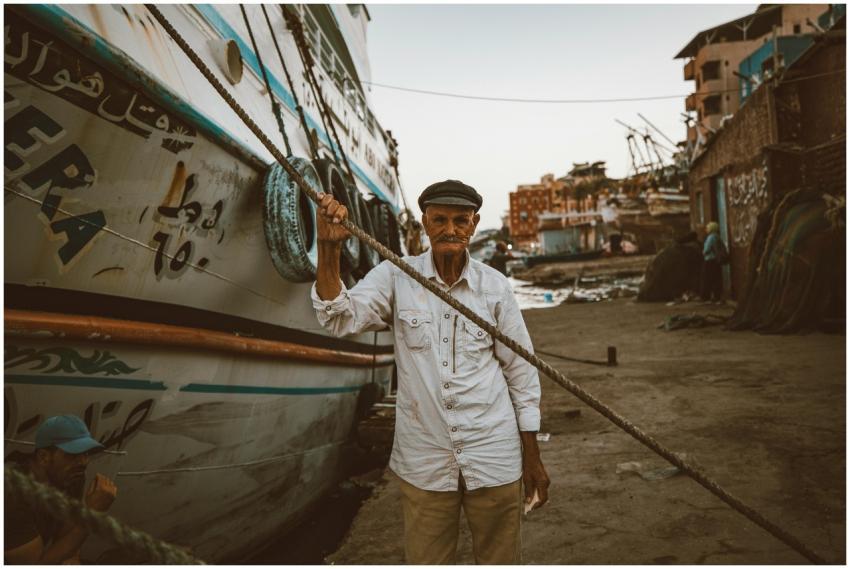 An elderly fisherman holding a rope near boats in