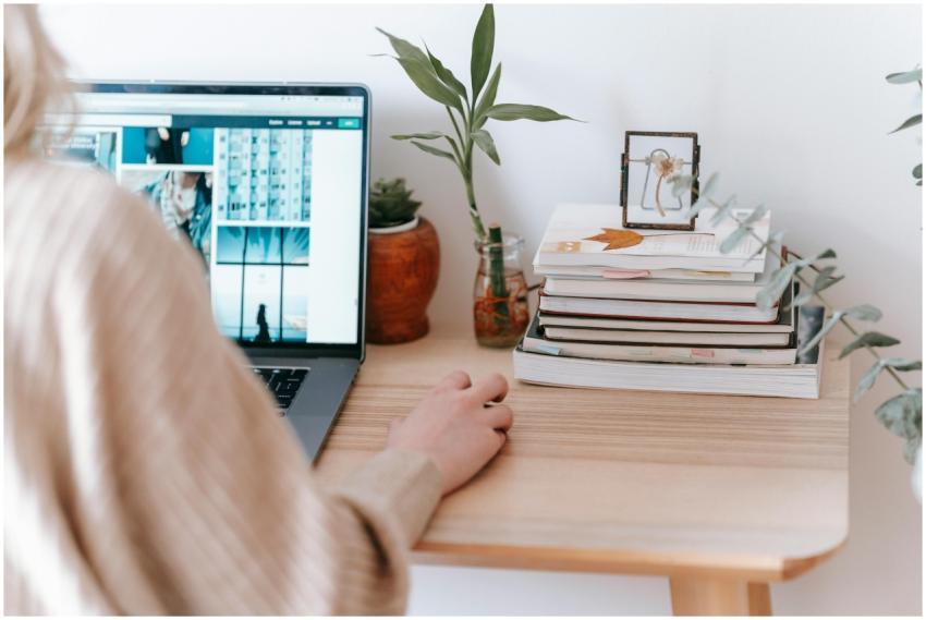 A woman using a laptop at home, surrounded by book