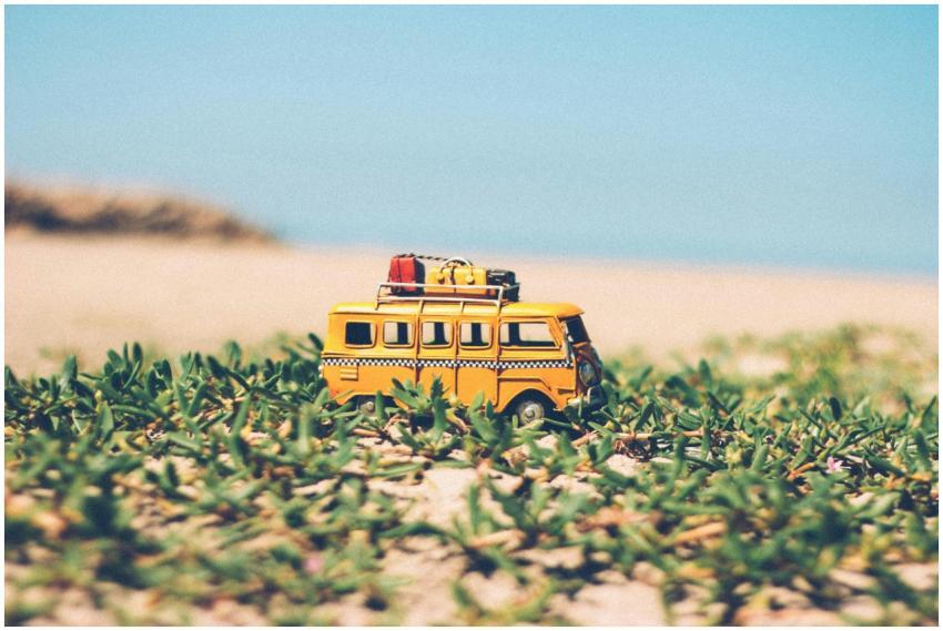 A toy yellow camper van on beach sand surrounded b