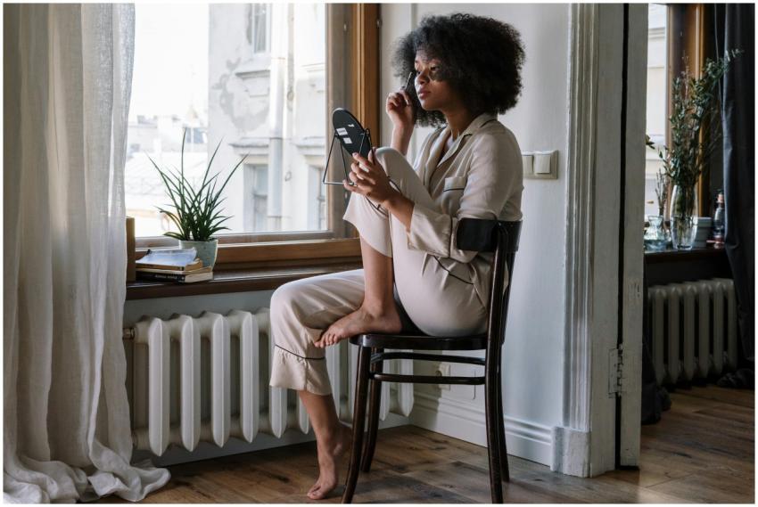 Woman in pajamas applying skincare with mirror, en