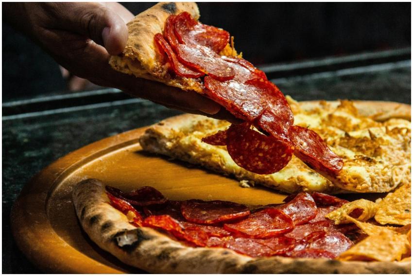 Fresh pepperoni pizza slice being lifted from a wo