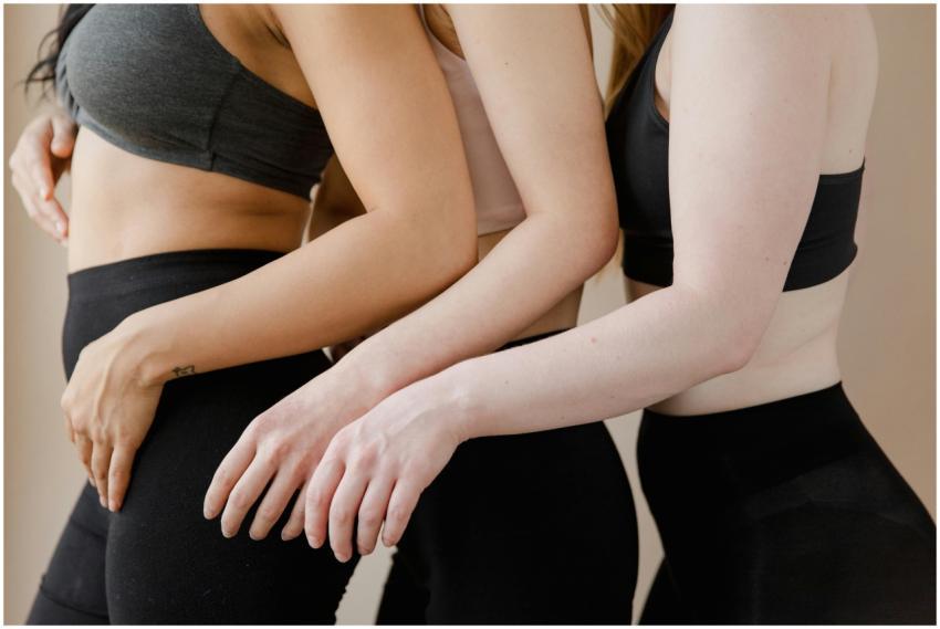 Three women in crop tops and leggings embracing bo