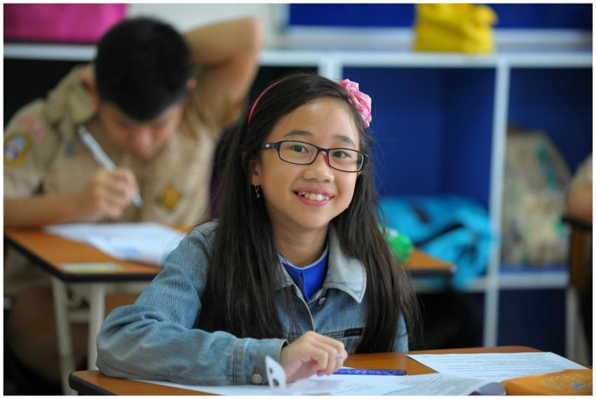 A young girl with glasses smiles while studying in