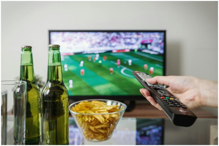 A person holding a remote while watching soccer on
