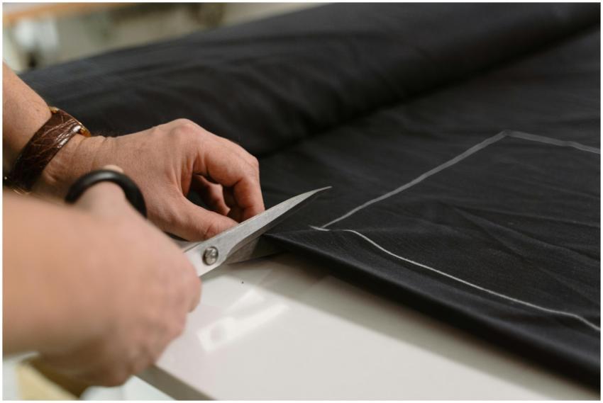 Close-up of a tailor's hand cutting black fabric w