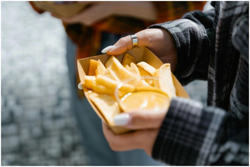 A close-up image of a person holding fries with di