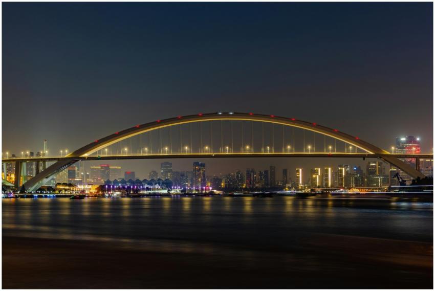 A night view of an illuminated bridge spanning a c