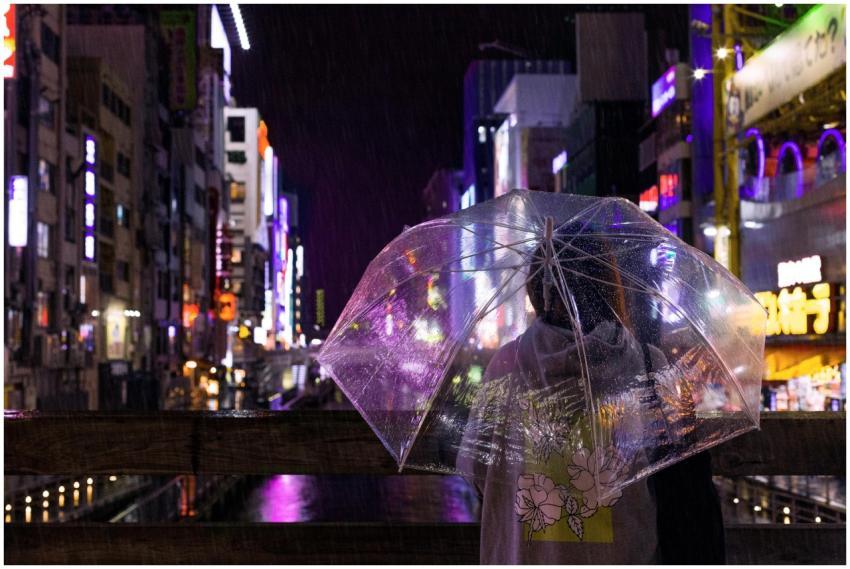 A person with an umbrella stands in a vibrant neon