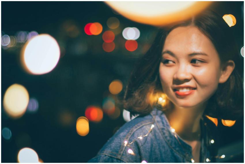 A young woman smiling surrounded by warm bokeh lig