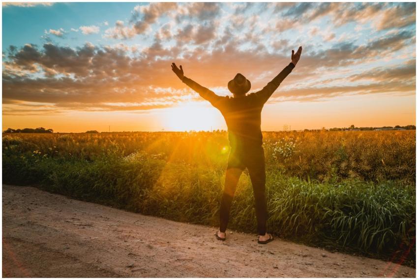 A man raises arms in freedom at sunrise in a rural