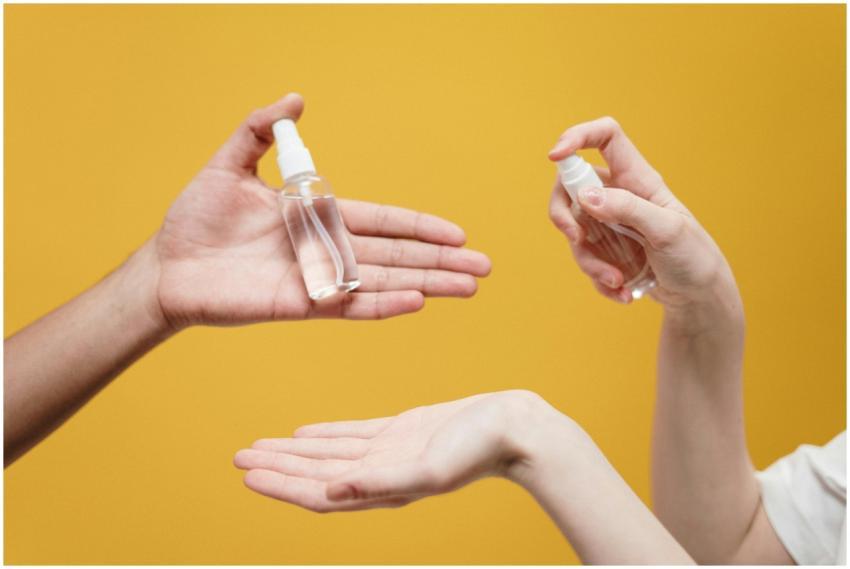 Hands using hand sanitizer against a yellow backgr