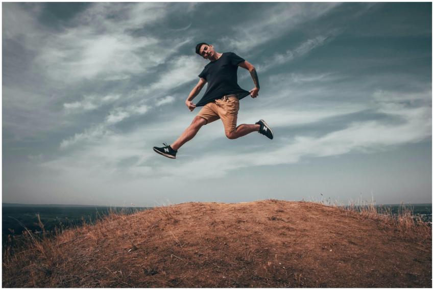 Young man jumping on a hilltop under a dramatic sk