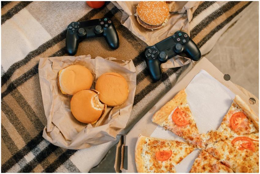 A top view of burgers, pizza, and gaming controlle