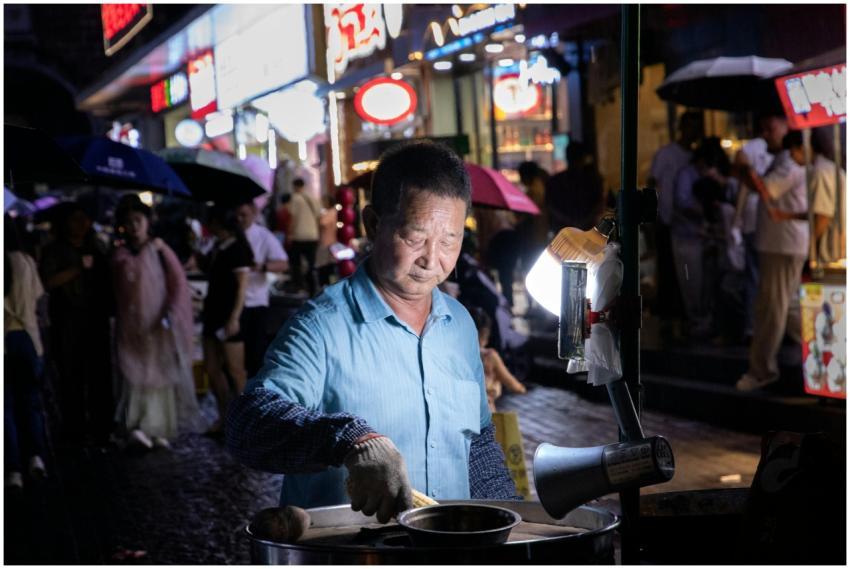 Street vendor in blue shirt cooks food at night in