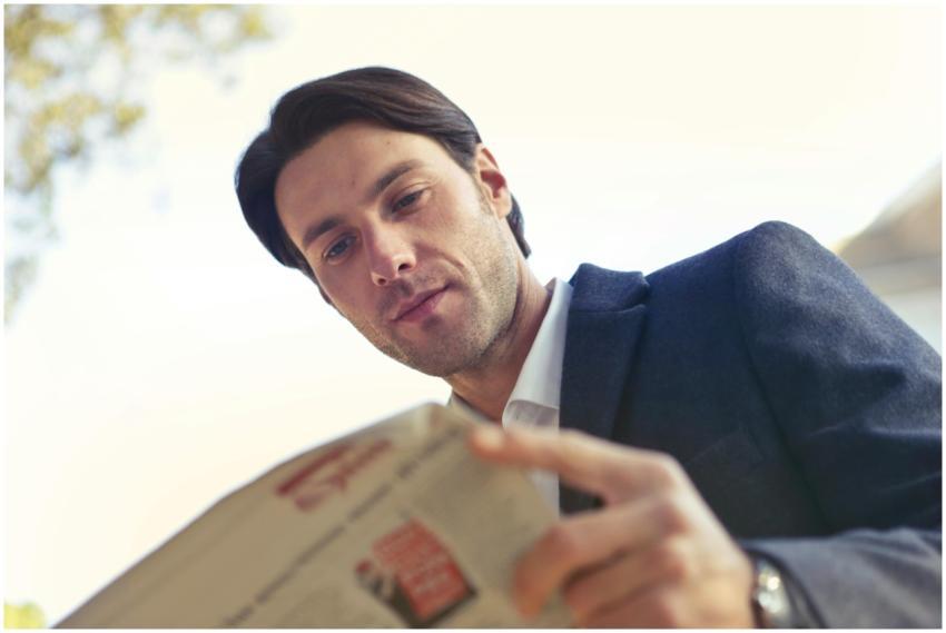 Adult man in formal attire reading a newspaper out