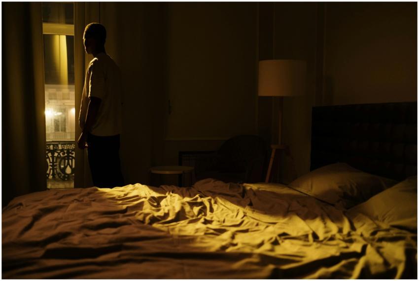 Man in dark bedroom gazing out window, highlightin