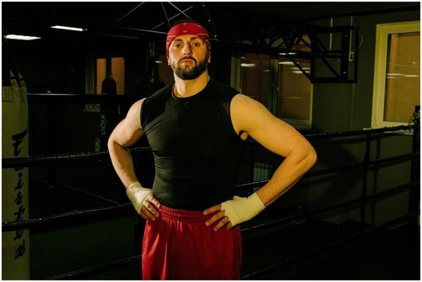 A male boxer in a black top and red shorts standin
