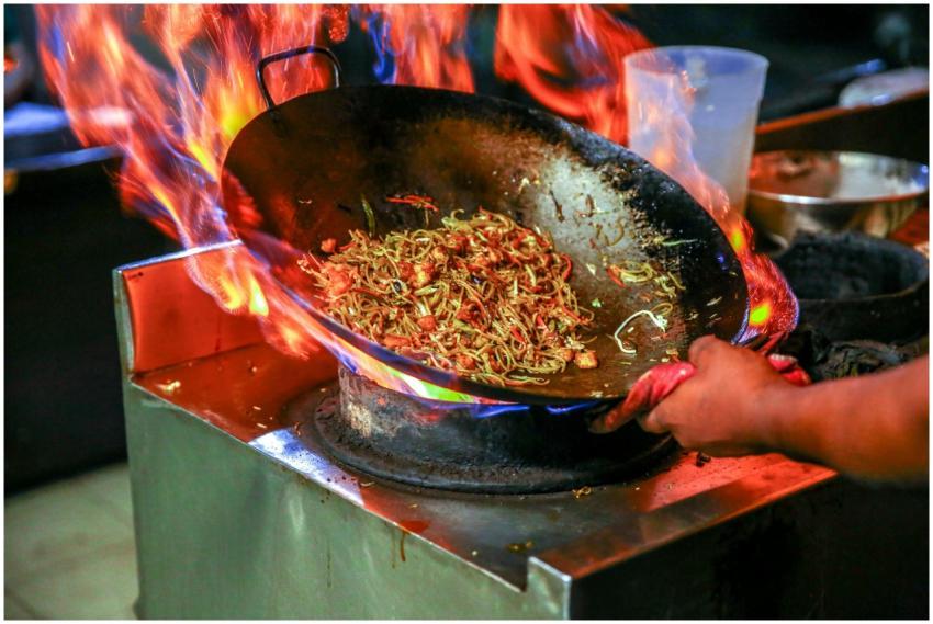 Vibrant close-up of chef cooking noodles in a flam