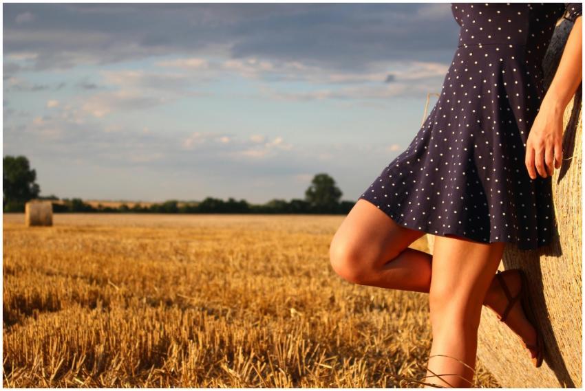A woman in a polka dot dress leans against a hay b
