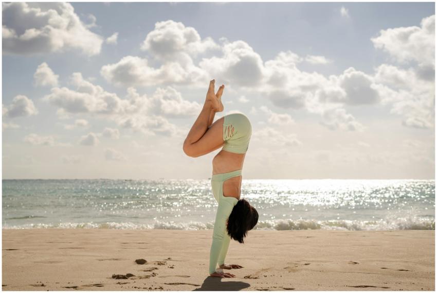 A woman in a handstand yoga pose on a serene beach