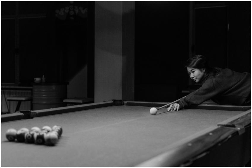 A woman skillfully plays billiards in a dimly lit