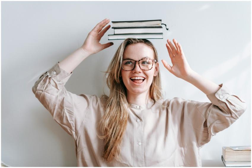 Smiling woman with glasses balancing books on her