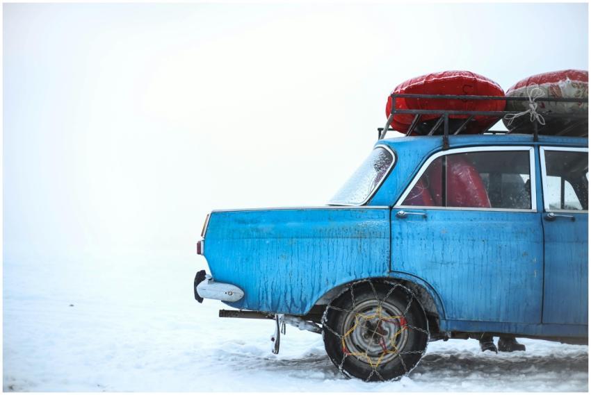 A vintage blue car with roof luggage in snowy Ak-T