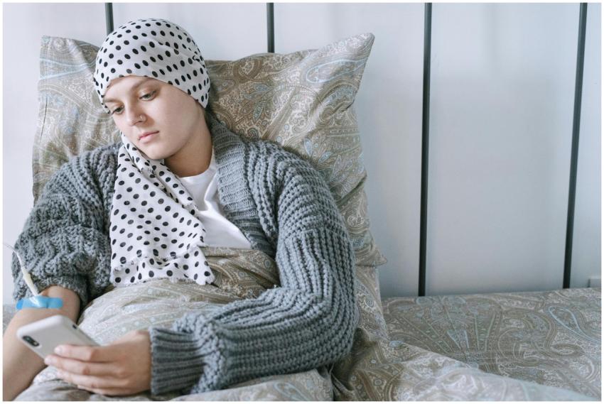 Woman resting in bed wearing a scarf, using her ph