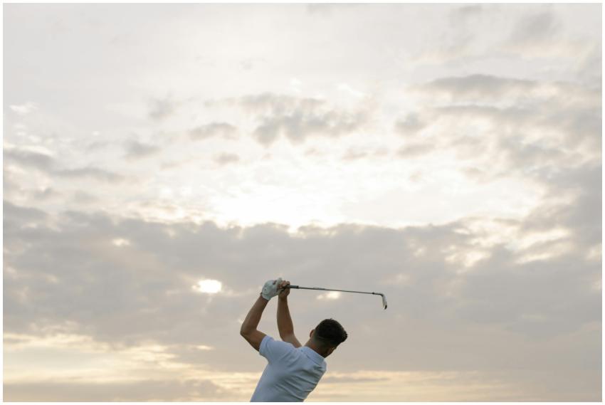 A golfer swings his club against a dramatic cloudy
