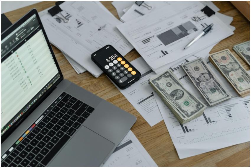 A desk with financial documents, currency, a lapto