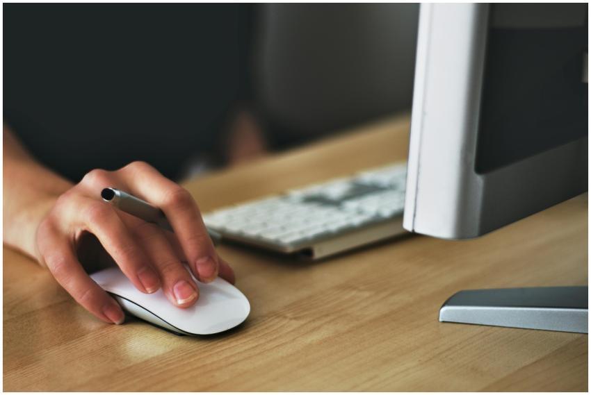 A hand using a wireless mouse at a modern desk set