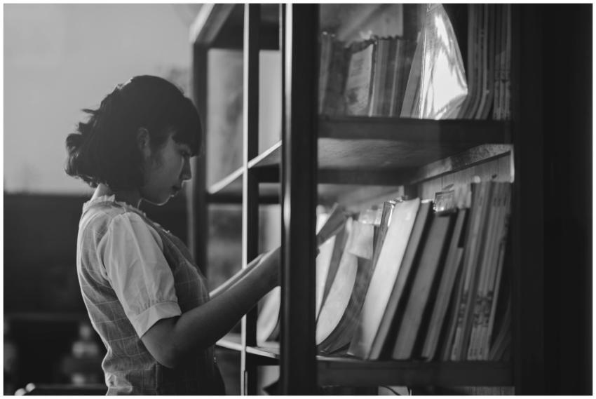 Side view of a woman reading books in a library, c