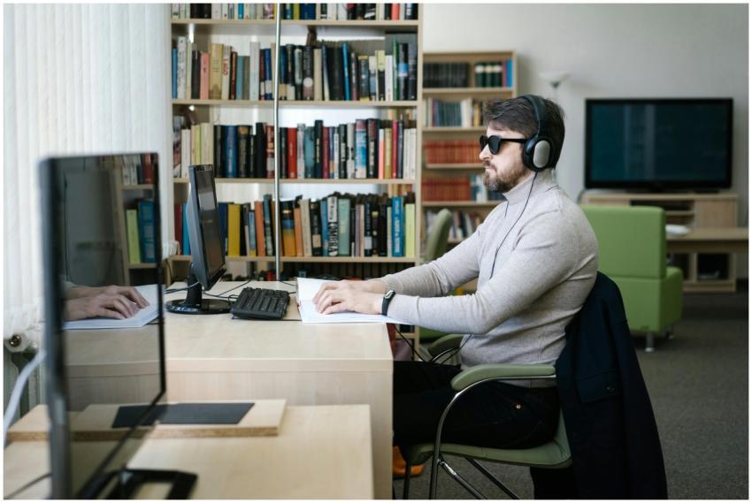 A blind man uses a computer with headphones in a l
