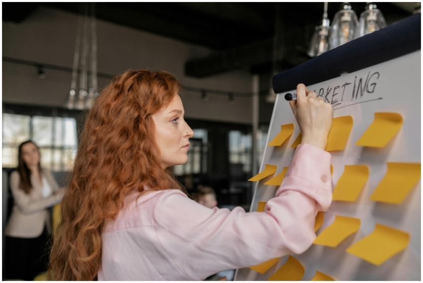 Red-haired woman writing on a whiteboard with stic