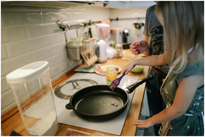 Young girl cooking with a frying pan under adult s