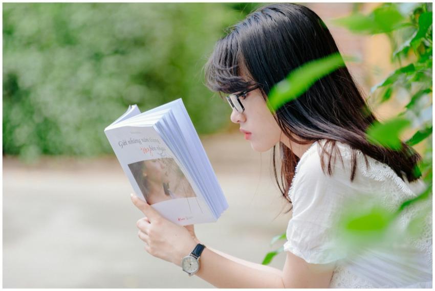 A young woman sits outdoors, absorbed in reading a