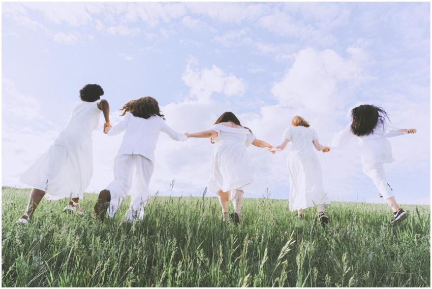 Five women joyfully running in a field under a cle